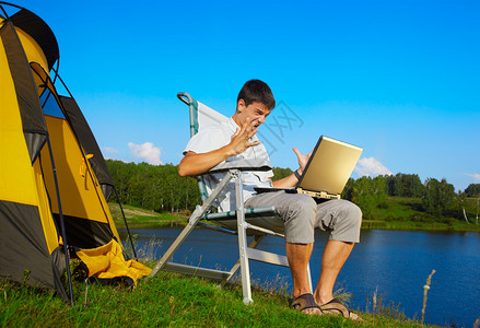 愤怒男子在露营帐篷室外坐在折叠椅上的笔记本电图片