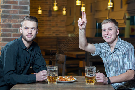 两个朋友在酒吧喝啤酒其中一个叫服务员来接客图片