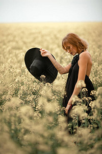身穿黑衣戴帽子的年轻女人在鲜花草地里图片