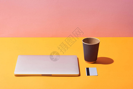 黄色表面和粉红背景的笔记本电脑和信用卡附近的纸面咖图片