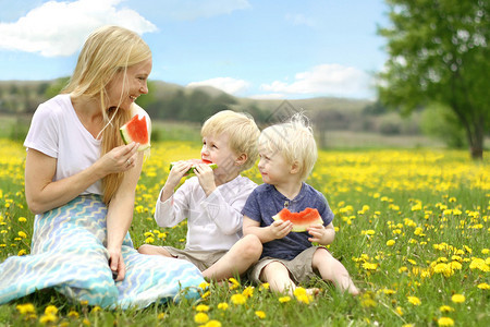 一位快乐的母亲和她的两个年幼的孩子坐在外边的花草地上图片