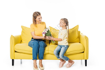 小孩在黄沙发上给妈送一束郁金香花孤立在白色的图片