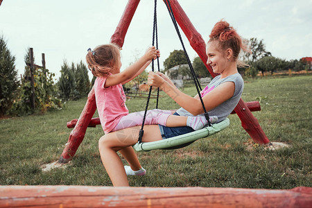 十几岁的女孩和她的妹在后院的家庭游乐场玩耍快乐微笑的姐妹们在夏日一起荡秋千真实的人图片