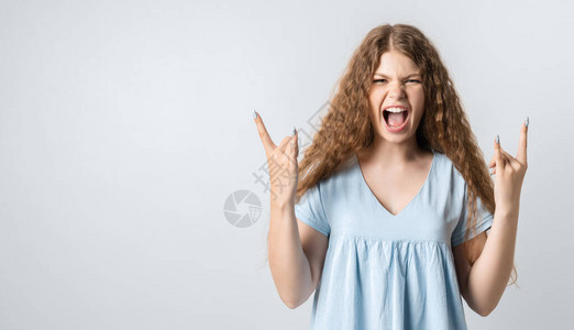 长卷发的情绪化欧洲年轻女做ROCKNROLL标志高清图片