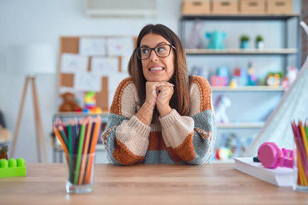 身着毛衣和眼镜的年轻美丽的女教师在幼儿园坐在办公桌旁笑紧张图片