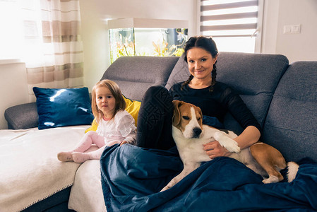 两岁大女儿的年轻母亲睡在明亮房间的沙发上宠爱狗图片