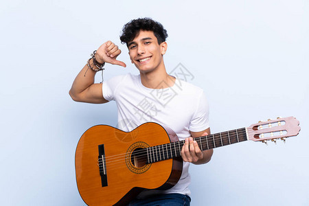 年轻阿根廷男子带着吉他与孤立的蓝色背景相伴图片
