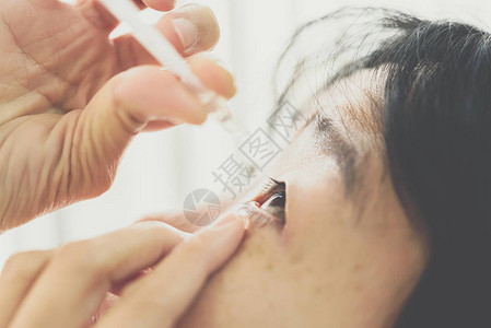 亚洲女使用滴眼液或人工泪液滴入眼部治疗眼球的炎症或干涩问题以图片