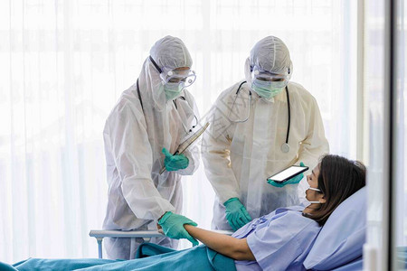 身着防护服和口罩的男女医生正在疾控区检查女患者的症状COVID19患者的护背景图片