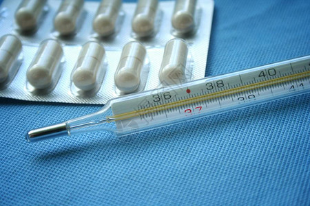 蓝色背景上的片剂药丸和水银温度计流感冒的概念医疗保健概念药背景图片