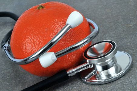 灰色背景上的听诊器和橘子特写背景图片