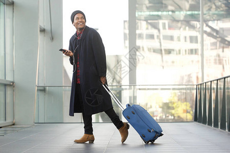 带着手机和行李在机场行走的笑旅行男子图片