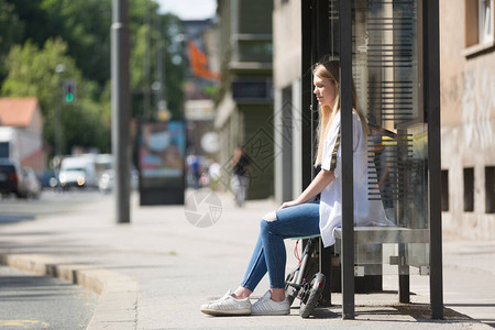 坐在公交车站点等车的年轻女孩图片