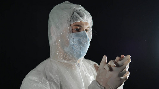 戴着医用口罩和防护服的医生在黑暗的背景下以慢动作为橡胶手套鼓掌支持医生对抗冠背景图片