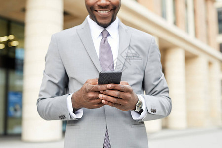 在城市里站着手机打字和微笑的非洲青年商人在手机上打字信息图片