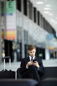 在机场候机室和复印空间要人休息室放松时使用智能手机的青年图片