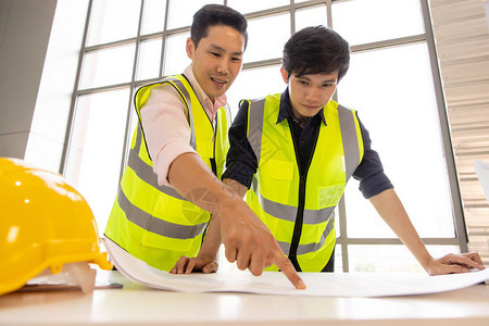 两位年轻英俊的亚洲工程师在建筑工地一起工作他们穿着亮黄色的安全反光衬衫男团队在现场和工厂一图片