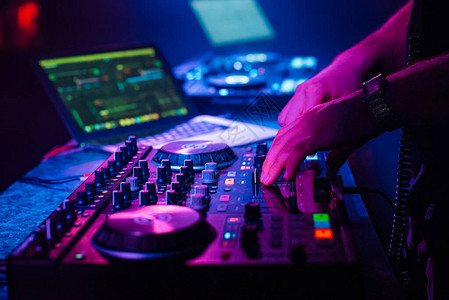 DJ把电子音乐和他手上的音乐控制板混在一起在夜总会的图片