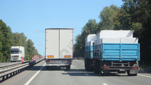 带白色货车拖的半卡车在郊区高速公路上超越装载的平板卡车图片