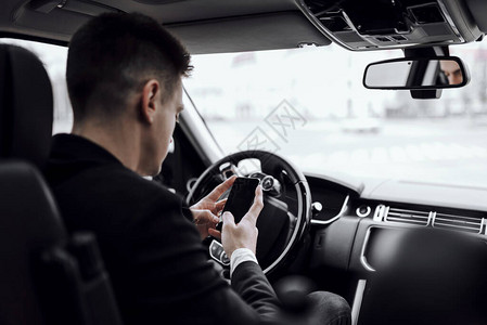 年轻商人在坐车时看智能手机屏幕的后视镜图片