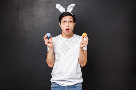 惊讶的年轻亚洲小伙在兔耳朵拿着彩蛋作为学习女朋友的传统背景图片