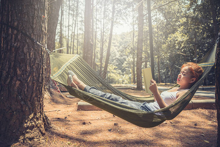 女人睡在吊床上看书在公园的自然大气图片