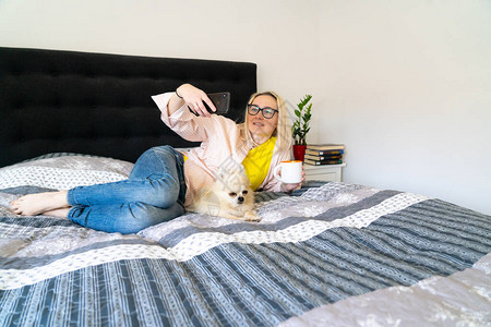 使用智能手机与朋友或家人进行视频通话的女女孩博主带着狗坐在卧室和追随者交谈Vlogger录制网络研讨会人坐在床上图片