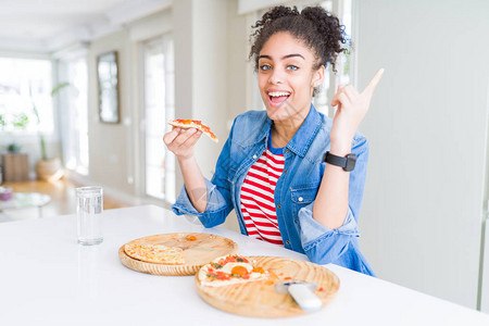 年轻非洲裔美国女人吃两条自制奶酪比萨饼非常快乐用手和指向图片