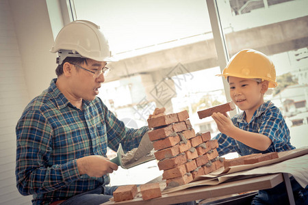 小男孩正在学习如何放下砖瓦工作从他的建筑工父亲图片