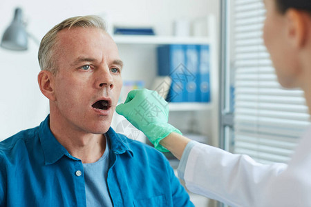 从成年男子口腔和喉部抽取样本的女医生在诊所复制空间进行测试图片
