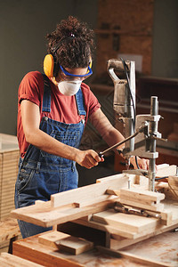 木工行业戴防护眼镜的年轻女木匠和护耳器在切割木板时按下木工图片