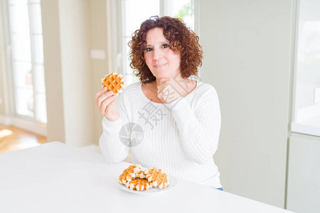 老年女人吃甜的贝吉安华夫饼面对严肃的面孔想着问题图片