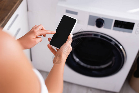 在自动洗衣机附近使用智能手机的年轻女子图片
