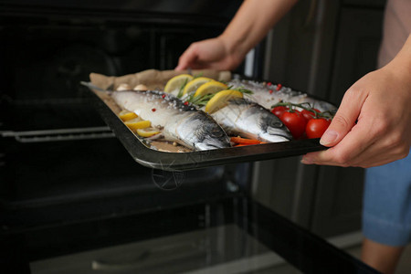 女人把装有生鲭鱼和蔬菜的托盘放进烤箱图片