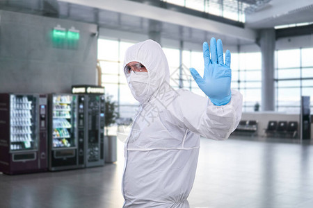 身着一次防疫抗菌隔离套装的男流行病学家在机场或火车站的候诊室中表背景