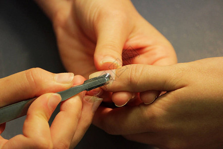 修指甲培训课程的学生先为一位女客户的手准备用刮刀的工具图片