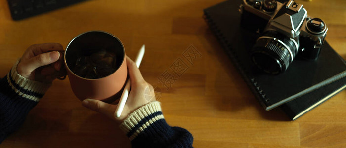 妇女自由职业者用日记笔本和照相机坐在工作空间时拿着咖啡杯图片