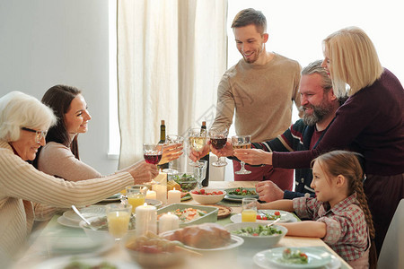 快乐的成熟和年轻家庭成员在圣诞节祝酒节期间与红酒交汇图片