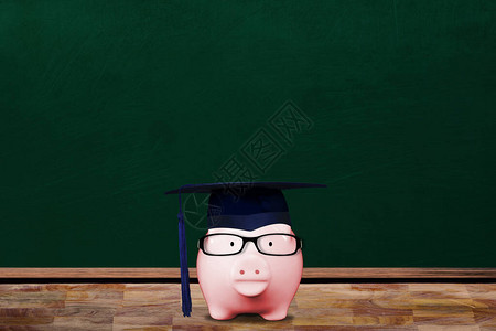 在学校教室里戴着研究生帽和眼镜的粉红色存钱罐为教育储蓄图片