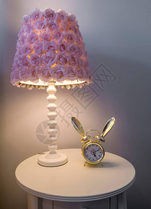 圆形边桌顶部的闹钟旁边有紫色花朵的灯罩关闭家庭卧室内的照图片