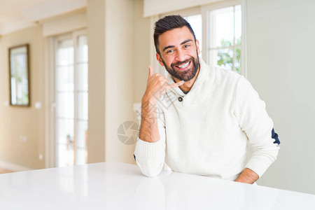 方向手势英俊的西班牙裔男子在家里穿着休闲的白色毛衣背景