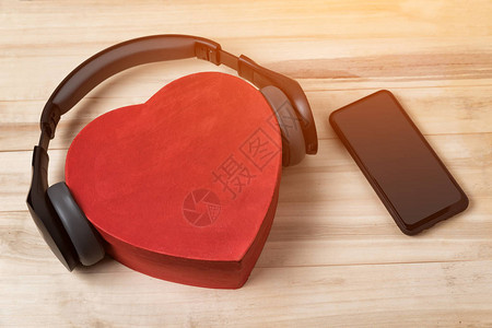 全尺寸无线耳机停在红心形盒子和浅棕色木制桌子上背景图片