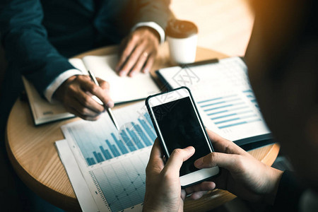 业务合作伙伴使用智能手机在办公室绘制公司财务报表告和利润工图片