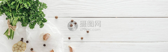 白色木桌上蒜瓣黑胡椒和欧芹的全景拍摄图片
