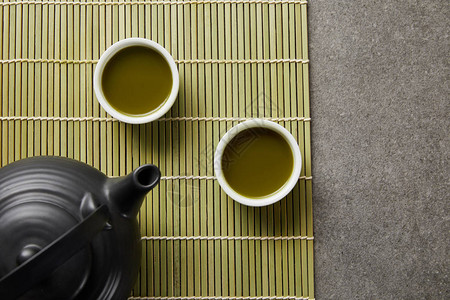 在竹桌垫上黑茶壶附近的青辣椒茶叶白图片
