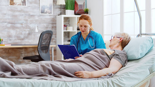 社会工作者咨询一位躺在病床上的老年残疾妇女看护人使用剪贴板记录养老金图片