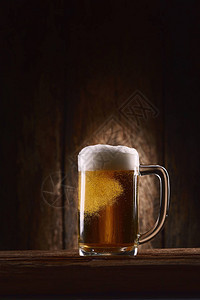 木制背景的木桌上的杯子里的啤酒图片