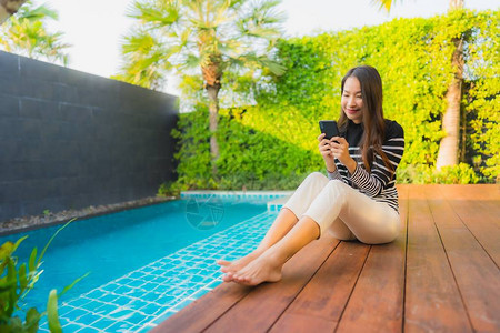 在旅馆度假胜地户外游泳池周围使用智能手机的年轻的图片