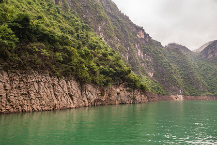 大宁河上的大雾或迷雾峡谷陡峭的斜坡与绿色植被和翡翠绿水附近裸露的棕色岩石表面带图片