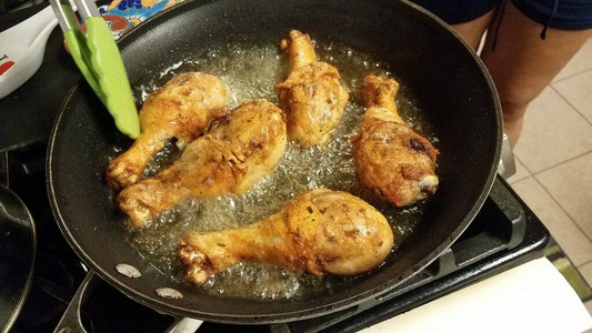 在炉子上的煎锅中用热油烹制的鸡腿图片